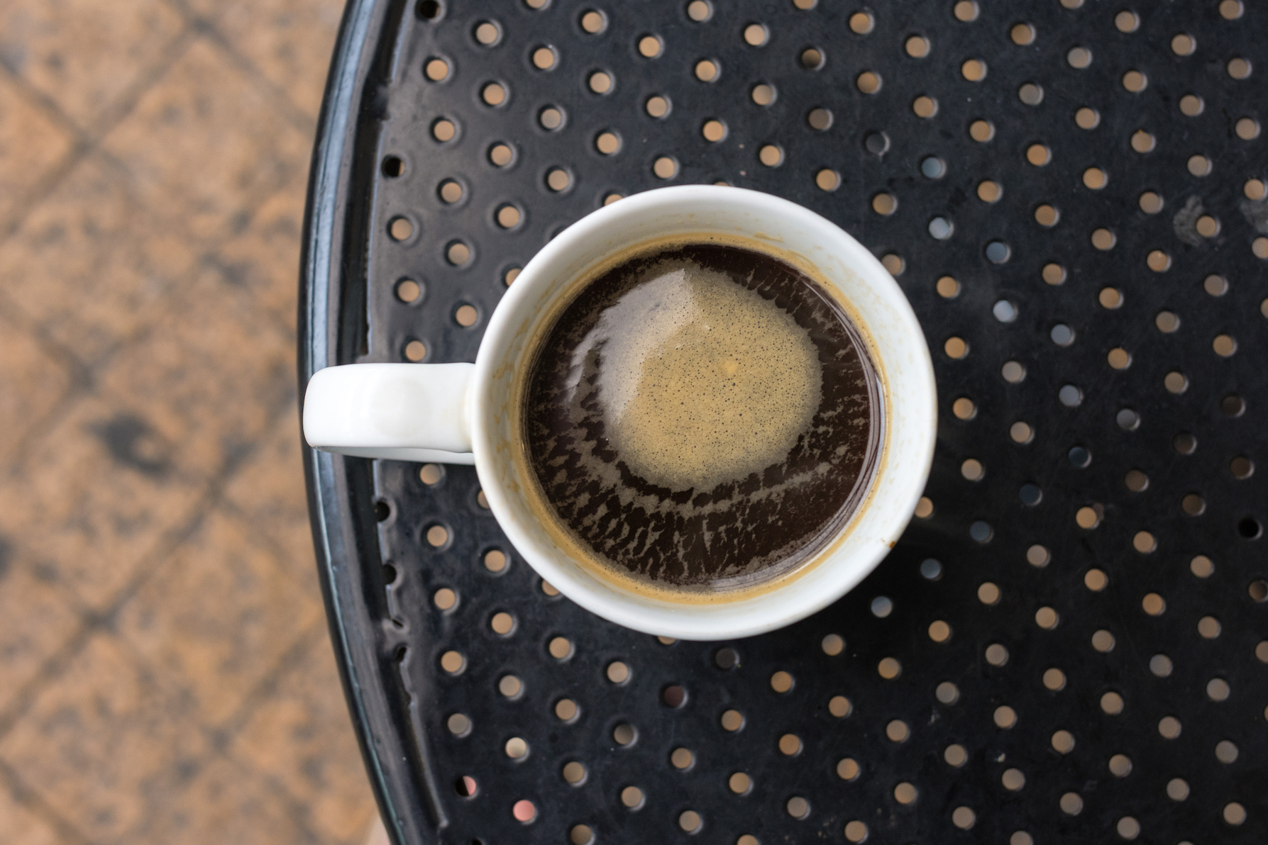 Americano coffee in standard white mug on black metal table from above.